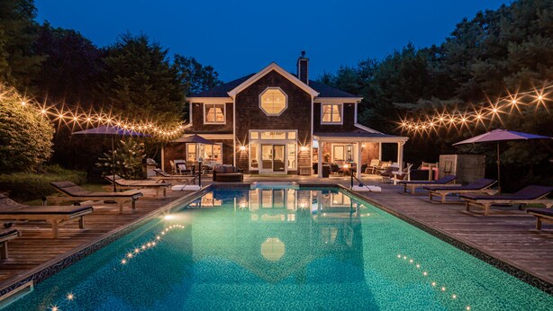 Une grande maison avec une piscine, des chaises longues et des guirlandes lumineuses.