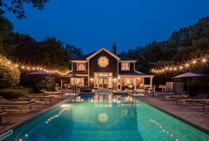 A large house with a swimming pool, deck chairs, and string lights.
