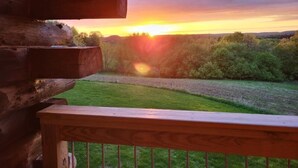 Una terraza de madera con vista a un atardecer sobre un campo cubierto de hierba y árboles.