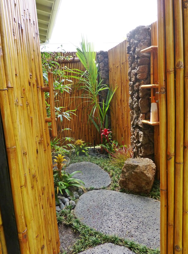 Una valla de bambú, un muro de piedra y un pequeño jardín con plantas y piedras para caminar.