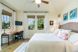 Un dormitorio con una cama grande, un escritorio, una silla, un televisor y un ventilador de techo.