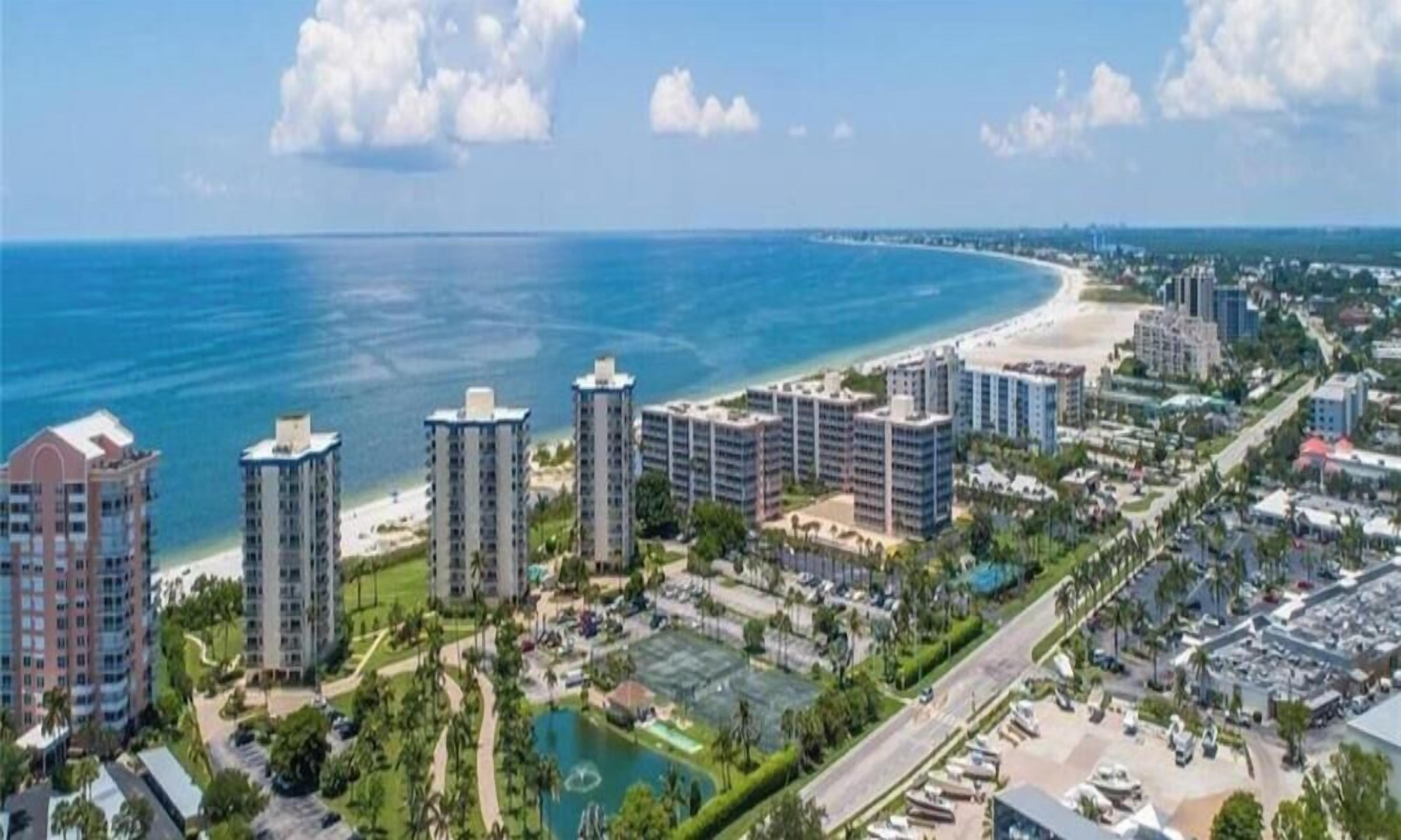 A coastal cityscape with high-rise buildings, a beach, and a marina.