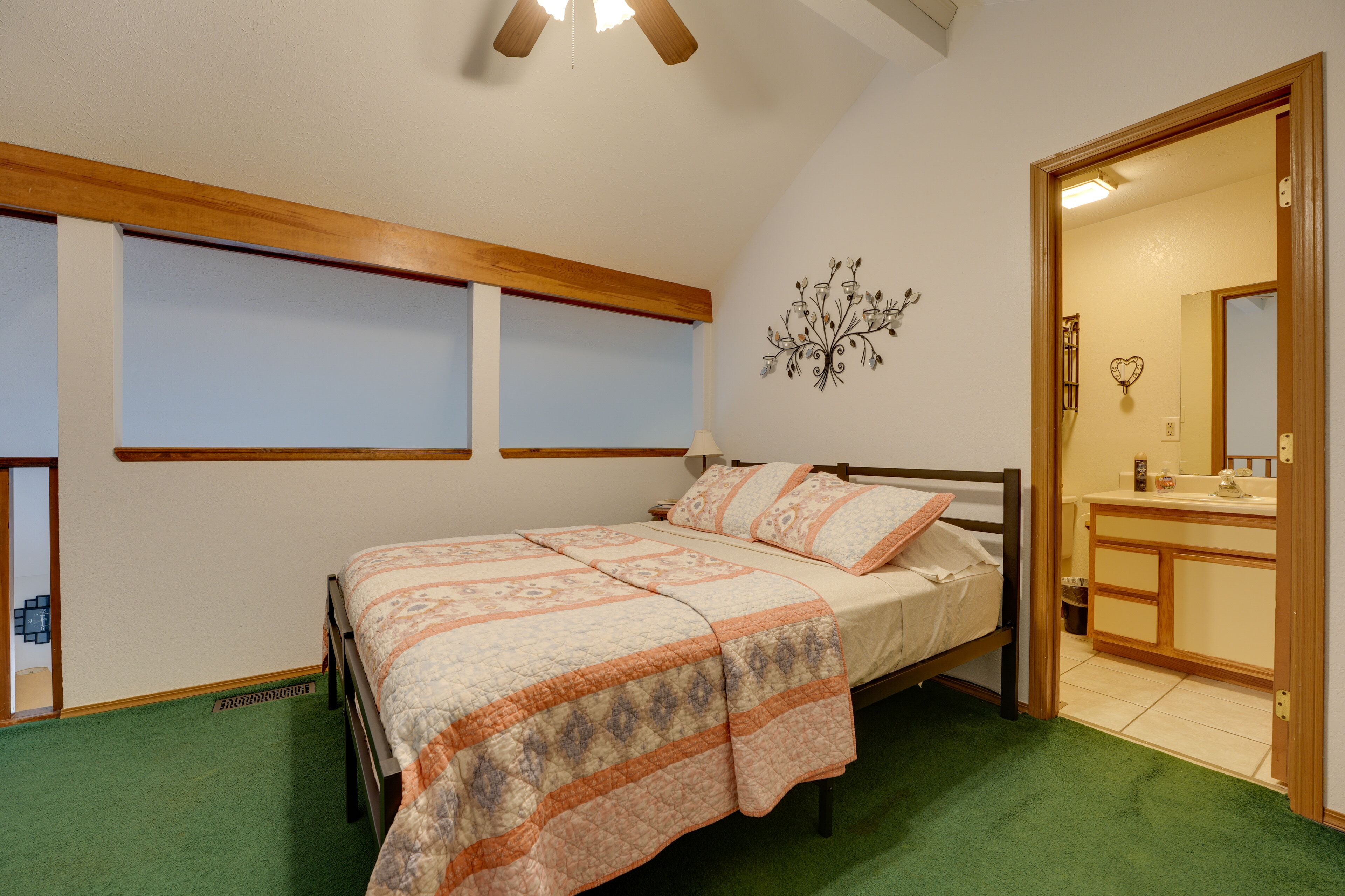 A bedroom with a bed, green carpet, wooden headboard, and a small window.