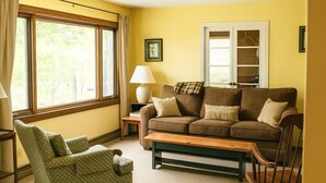 A cozy living room with a brown sofa, a green armchair, a wooden bench, and a lamp on a side table. - Chesapeake on Parker Lake (Oxford)