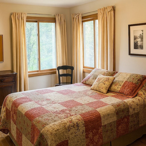 A bedroom with a large bed, two windows with curtains, a chair, a dresser, and a framed picture on the wall.