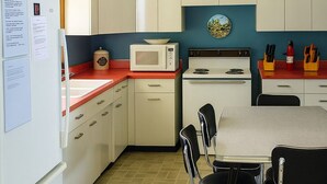A compact kitchen with white cabinets, a microwave, a stove, and a dining area with a table and chairs. - Chesapeake on Parker Lake (Oxford)