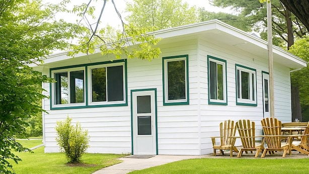 A small, single-story house with a white exterior and green trim, a front door, and a small front yard with a lawn and a few trees. - Chesapeake on Parker Lake (Oxford)