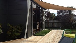 A wooden deck with a small grassy area, a sliding door, and a yellow and green chair.
