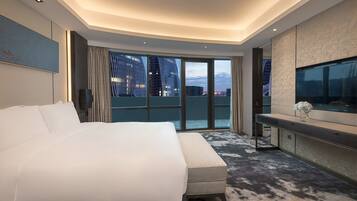 A modern hotel room with a large bed, a TV, a balcony with a view of the city, and a large window.
