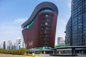 A modern hotel with a curved facade, multiple floors, and a prominent entrance area with a fountain. - Holiday Inn Nanjing South Station by IHG (Nanjing)