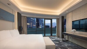 A modern hotel room with a large bed, a sofa, a TV, and a balcony with a city view. - Holiday Inn Nanjing South Station by IHG (Nanjing)