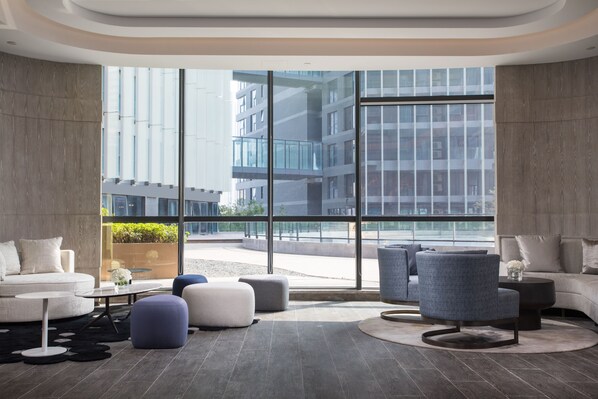 A modern hotel lobby with a large window offering a view of a cityscape. There are sofas, ottomans, and a coffee table. - Holiday Inn Nanjing South Station by IHG (Nanjing)