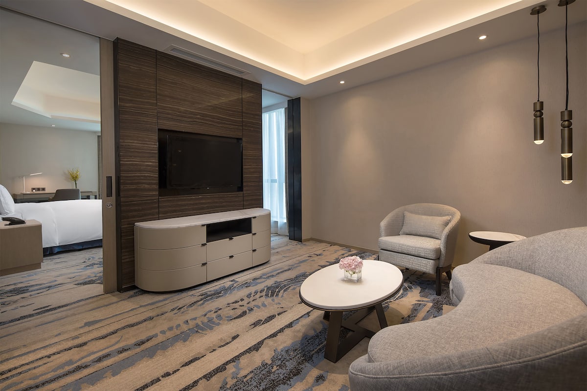 A modern hotel room with a large flat-screen TV, a sofa, a round coffee table, and a small side table.