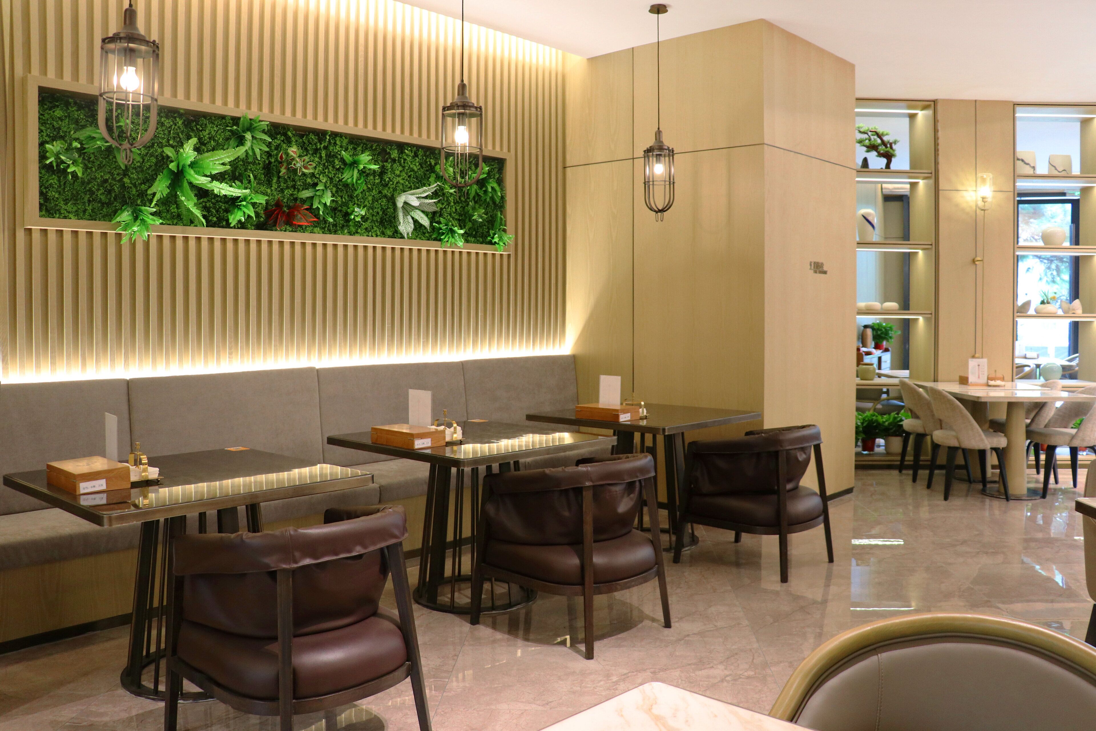 A modern restaurant with a long counter, leather chairs, and a green wall with plants.
