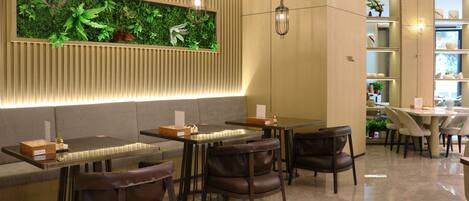 A modern restaurant with a long counter, leather chairs, and a green wall with plants.