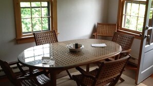Een ronde glazen tafel met een geweven stoel, omringd door ramen met uitzicht op groen.