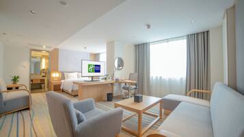 Une chambre d’hôtel comprenant un lit, un bureau, un ordinateur, une chaise, un canapé et une grande fenêtre avec des rideaux.