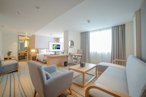 Habitación de hotel con cama, escritorio, computadora, silla, sofá y ventana grande con cortinas.