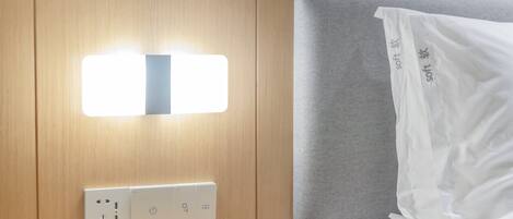 Ein Hotelzimmer mit einem hölzernen Kopfteil, einem Nachttisch mit Steckdose und einem weißen Kissen mit dem Aufdruck 'soft'.