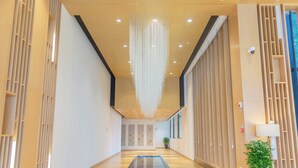 A modern hotel lobby with a glass partition, wooden paneling, and a hanging light fixture.
