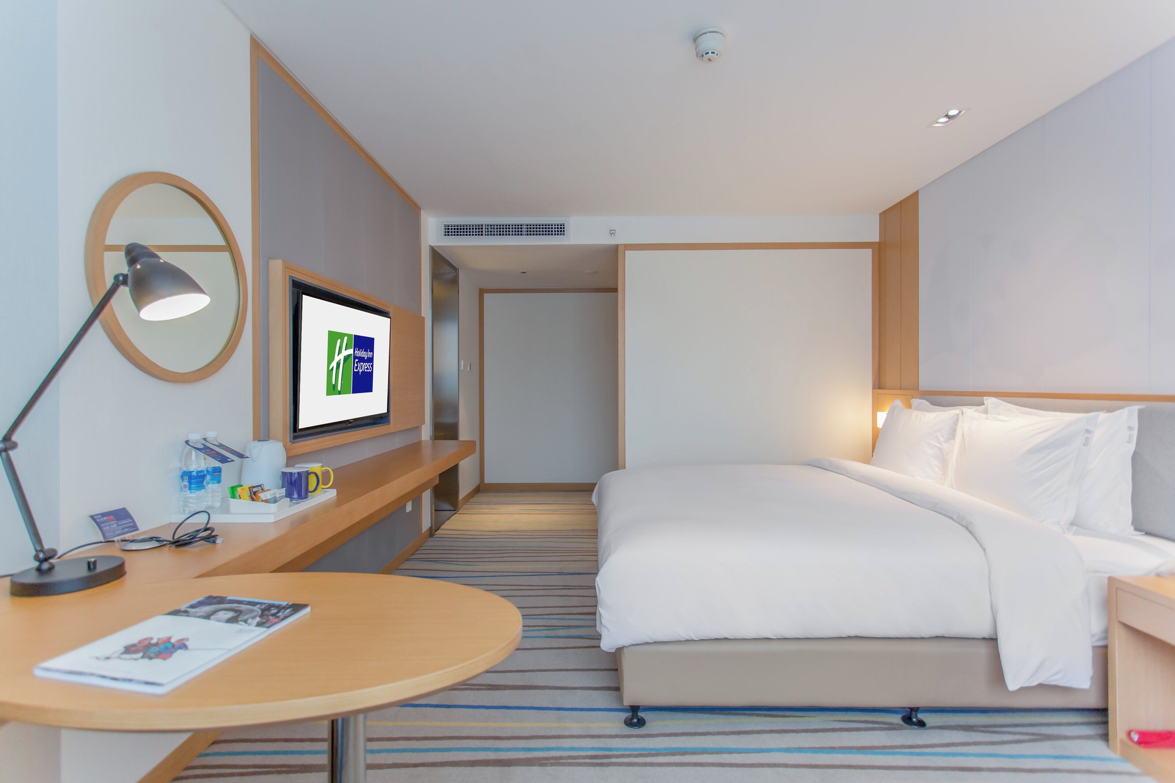 Habitación de hotel con cama, escritorio con lámpara, televisor y espejo montado en la pared.