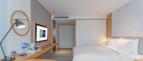 Habitación de hotel con cama, escritorio con lámpara, televisor y espejo montado en la pared.