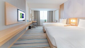 Una habitación de hotel con cama, escritorio, silla y televisor en la pared.