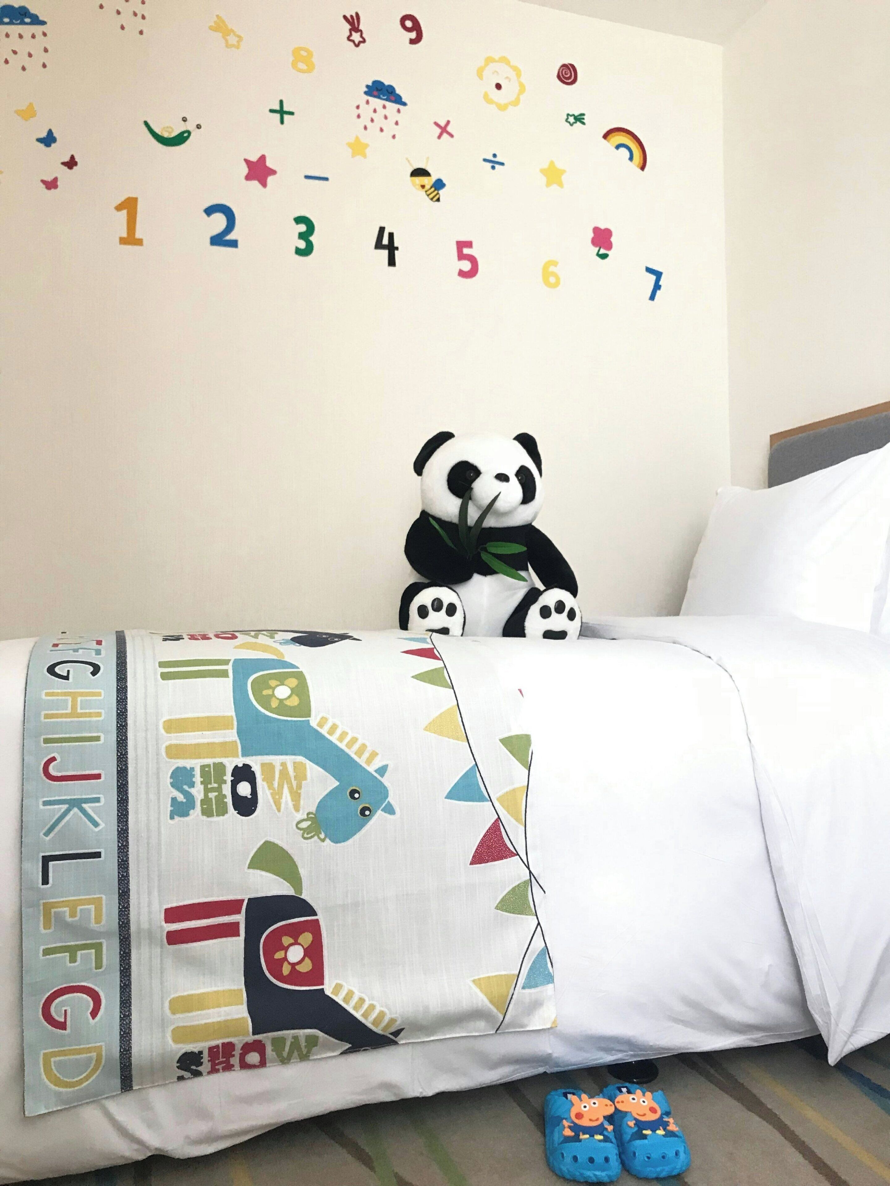 Ein Kinderzimmer mit einem Bett, einem Panda-Plüschtier, Buchstaben-Wandstickern und einem farbenfrohen Kissen.