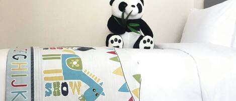 Ein Kinderzimmer mit einem Bett, einem Panda-Plüschtier, Buchstaben-Wandstickern und einem farbenfrohen Kissen.