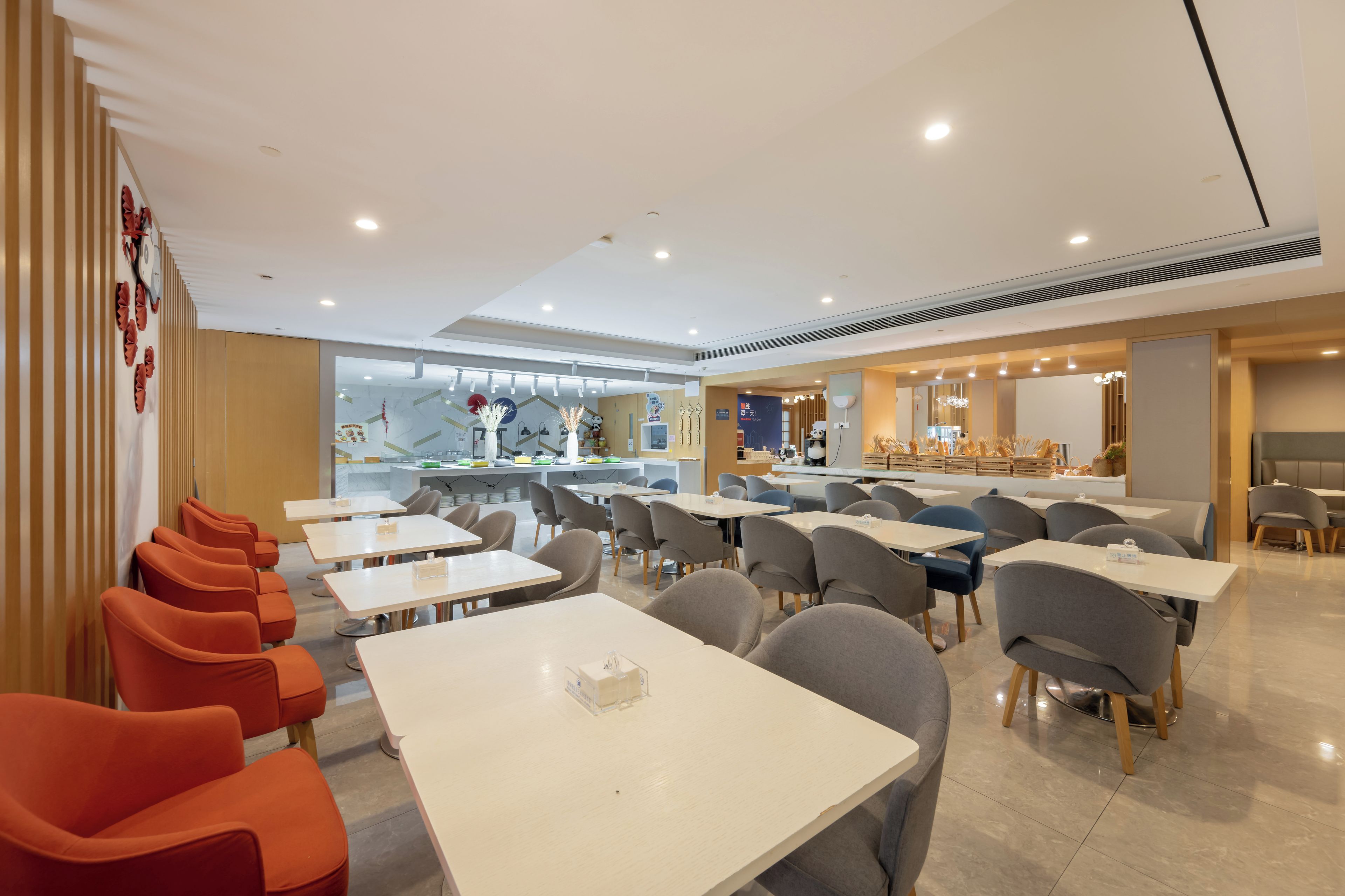 Un espace repas moderne avec des tables et des chaises, un comptoir où sont présentés des aliments, et un mur décoratif.