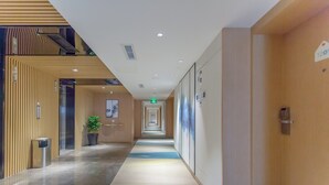 Un pasillo moderno de hotel con un largo corredor, una planta en maceta y un cartel que indica la habitación 1201.