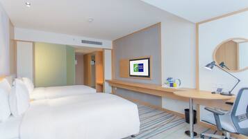 Habitación de hotel con cama, escritorio, silla, lámpara de escritorio, ordenador y televisor.