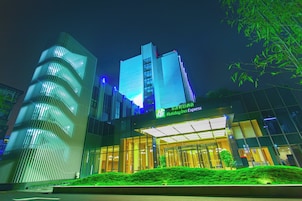 Um edifício moderno com a placa do Holiday Inn Express, com fachada de vidro e uma estrutura cilíndrica distinta à esquerda.