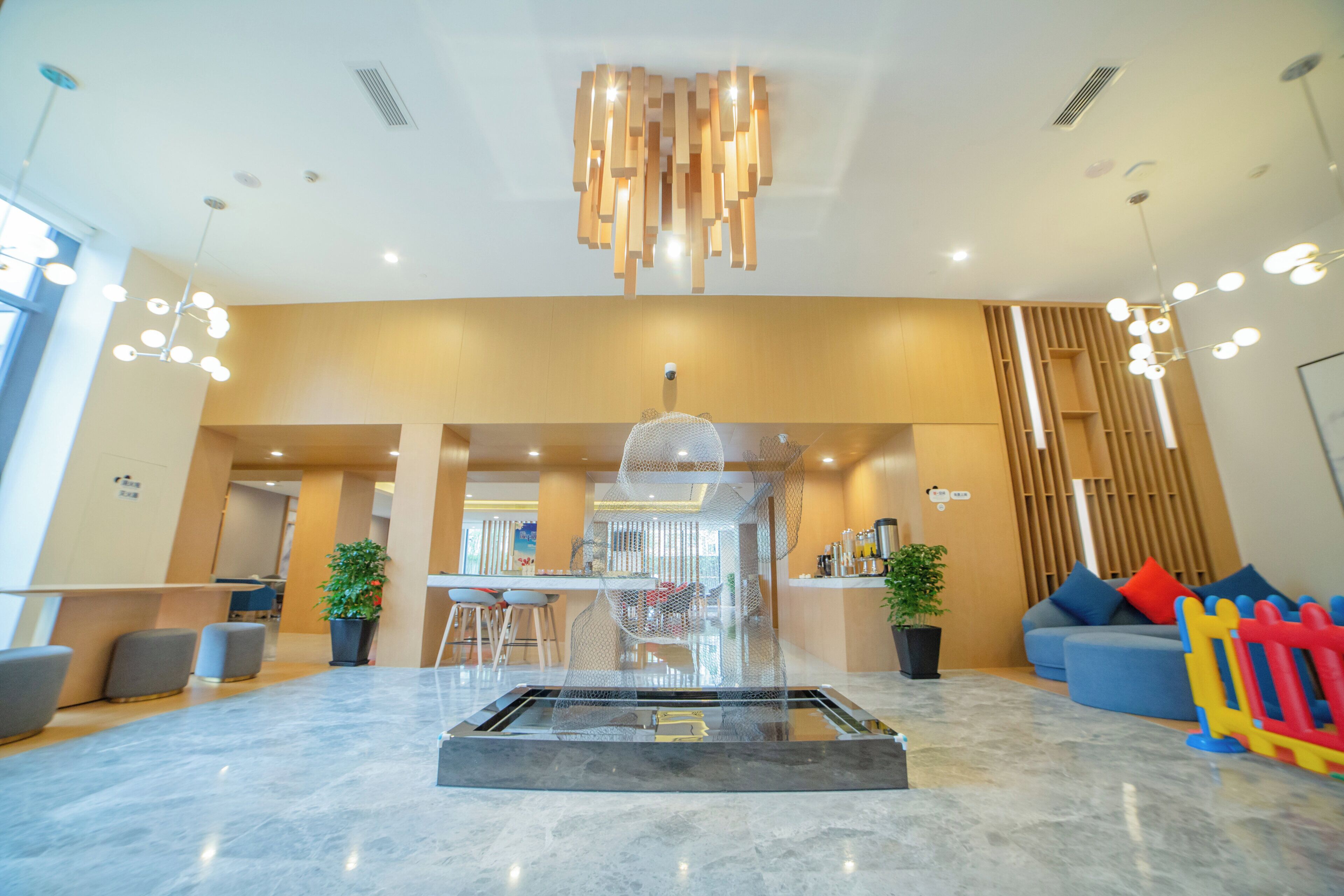 Een moderne lobby met een centrale glazen tafel, zithoekjes en een decoratieve plafondlamp.