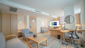 Habitación de hotel moderna con sofá, sillón, escritorio y televisor que muestra un mensaje.