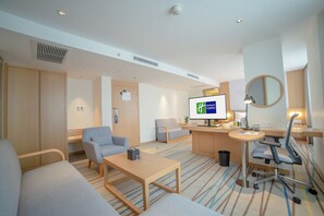 A modern hotel room with a sofa, armchair, desk, and a television displaying a message. - Holiday Inn Express Ya'An City Center by IHG (Ya'an)