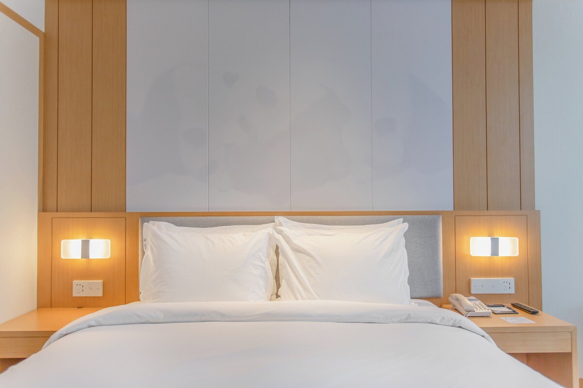 A neatly made bed with white linens, two bedside lamps, a bedside phone, and a nightstand.