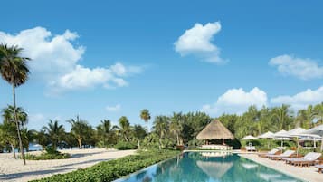 A poolside area with lounge chairs, a thatched-roof structure, and palm trees.