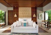 A modern bedroom with a large bed, wooden ceiling, and a view of greenery outside.