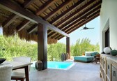 A covered outdoor area with a pool, wicker furniture, and a view of greenery.