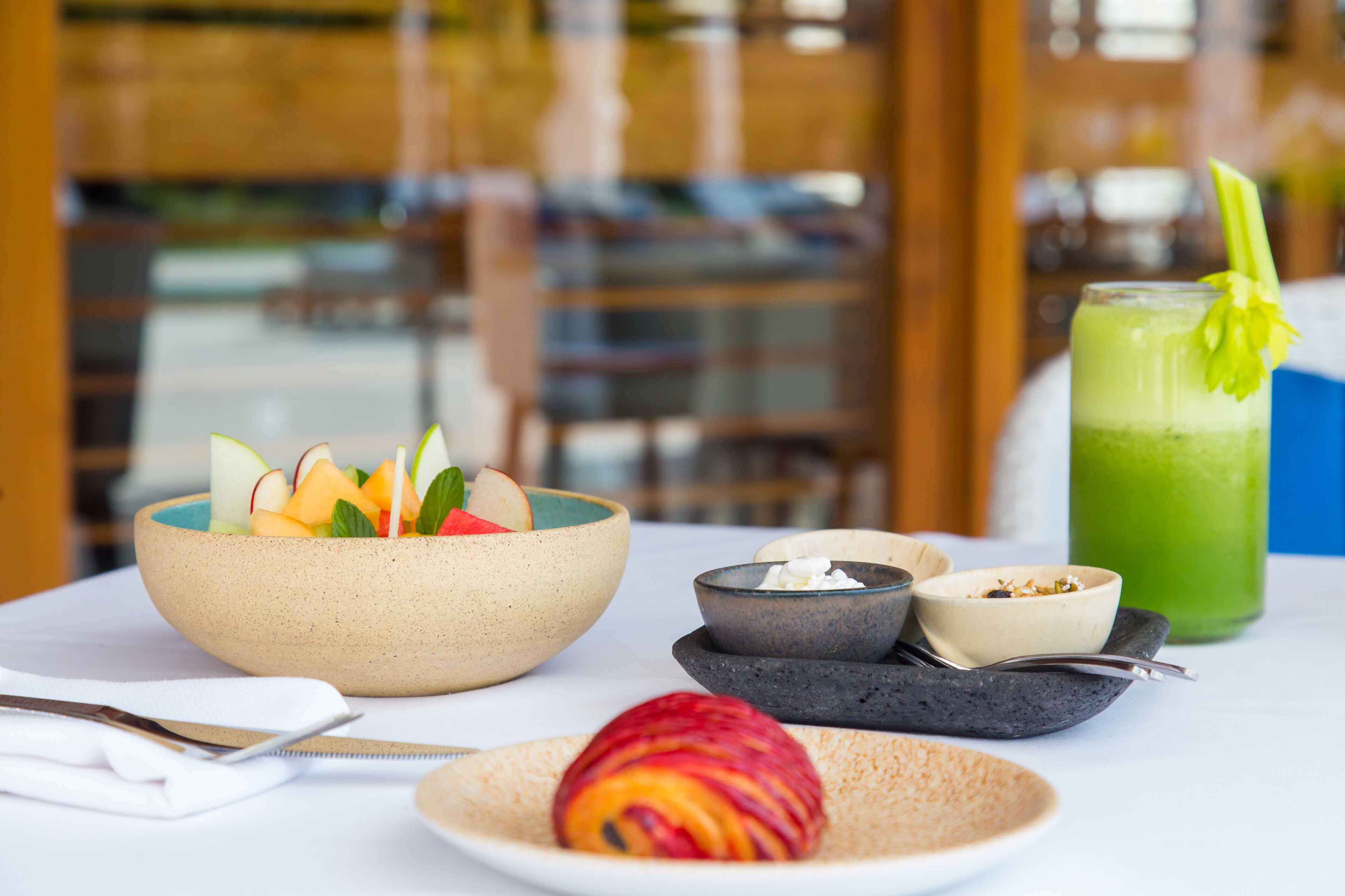 A table with a fruit bowl, a plate with a fruit, a green drink, and small bowls with food items.
