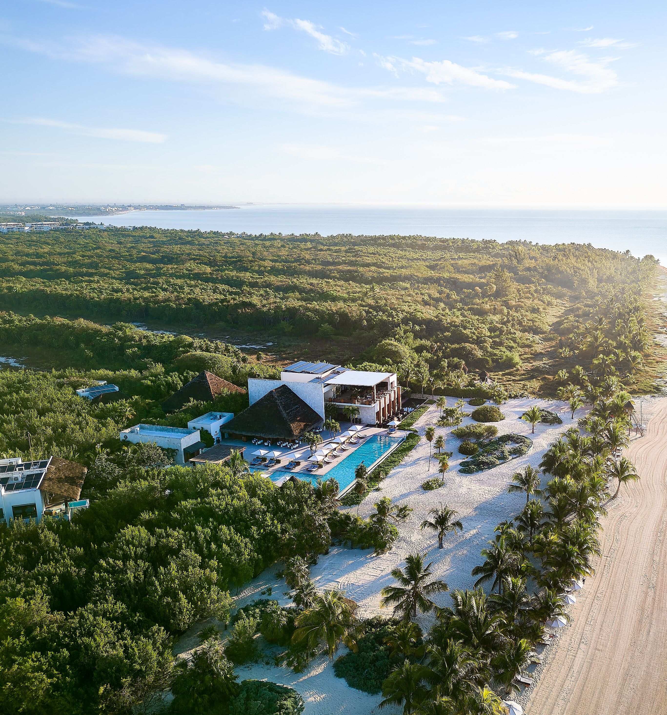 An aerial view of a resort with a swimming pool, beach, and dense forest.