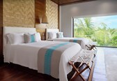 A hotel room with two beds, a large window with a view of palm trees, and a woven wall design.