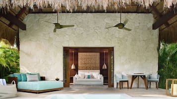 Una habitación con pared de piedra, techo de paja, un sofá, una mesa, sillas y una piscina.