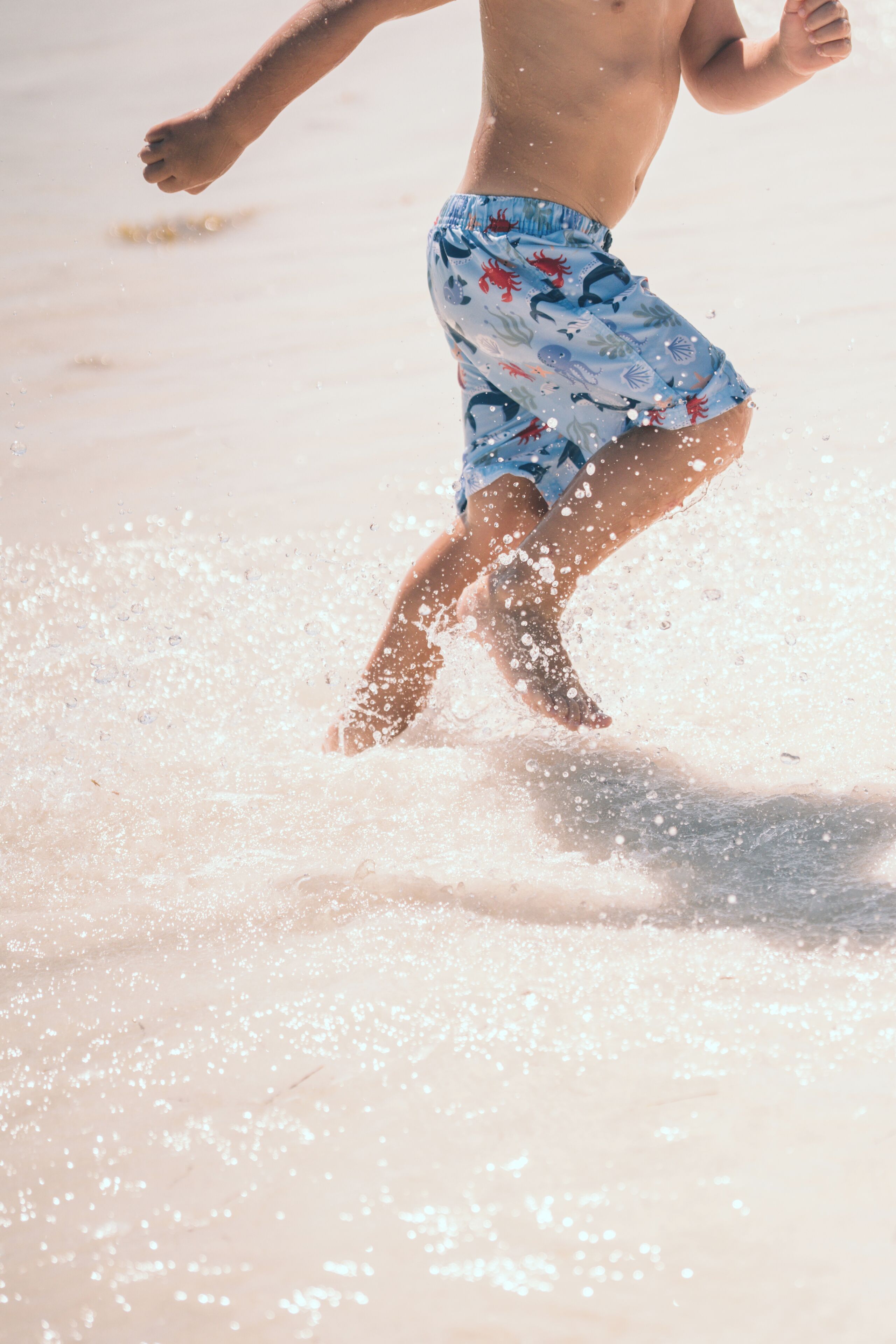 Una persona con shorts de baño caminando sobre la playa.