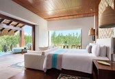 A spacious bedroom with a large bed, a sitting area, and a view of greenery outside.