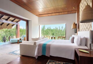 A spacious bedroom with a large bed, a sitting area, and a view of greenery outside.