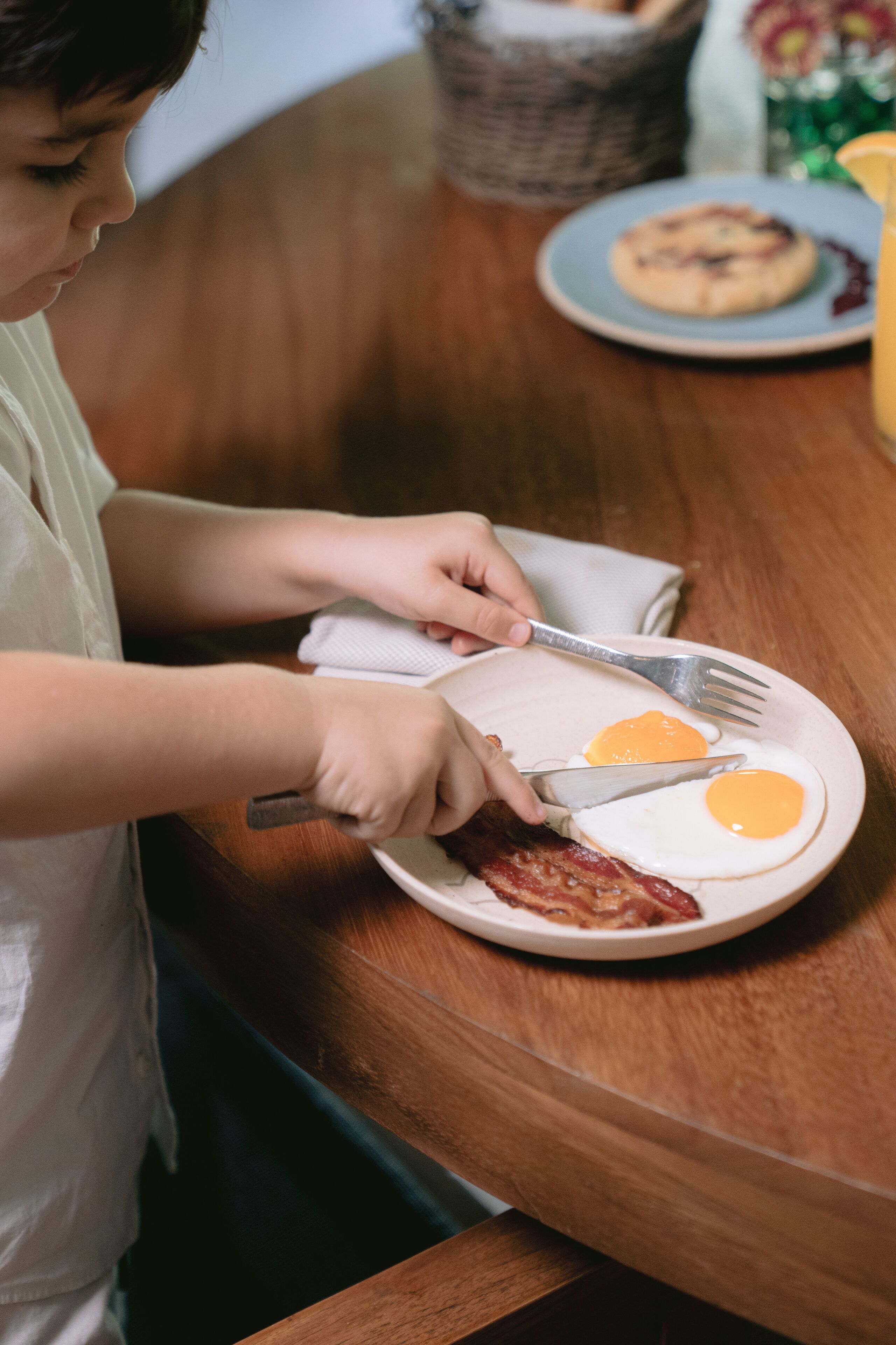 A person preparing breakfast with eggs and bacon on a plate.