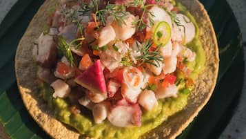 Un plato con una tortilla cubierta de guacamole, tomates picados, cebollas y hierbas.