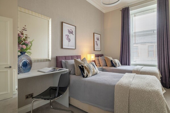 A hotel room with two beds, a desk with a chair, a mirror, and artwork on the wall.